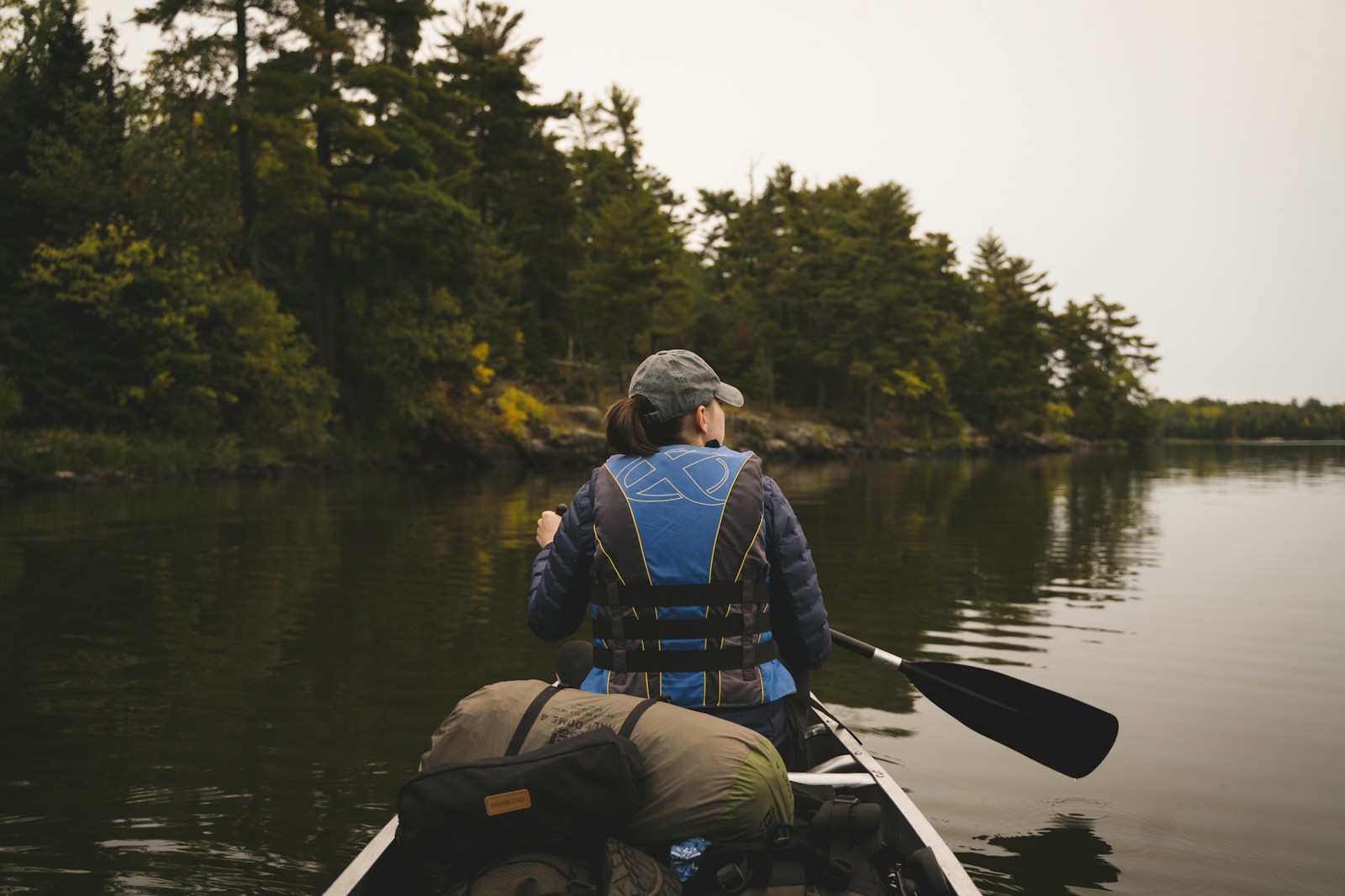 Homme en veste bleue et sac à dos noir faisant du kayak sur une rivière pendant la journée.