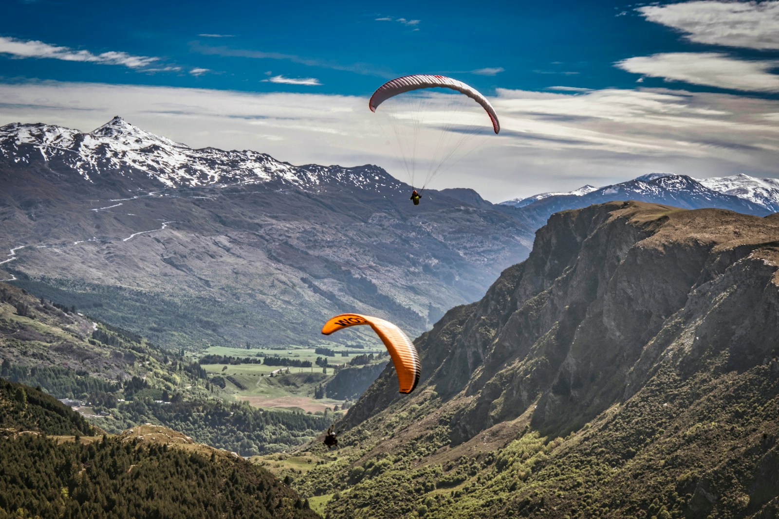 Une personne en parachute jaune survolant les montagnes en plein jour.